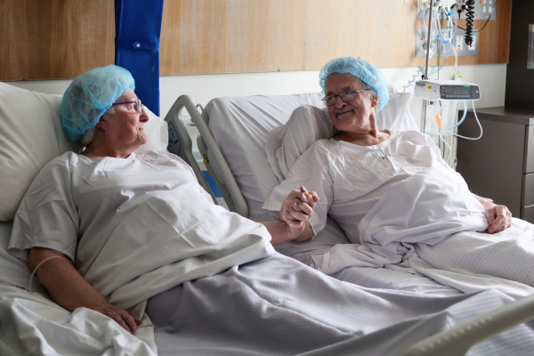 Margaret and Gary hold hands while in adjacent hospital beds in Austin Hospital as they prepare for living donor kidney transplantation
